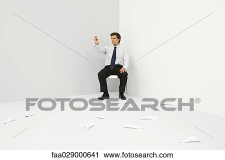 Stock Image - Male professional sitting in corner, throwing paper airplanes. Fotosearch