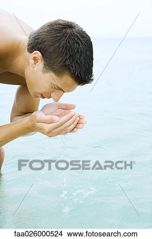 Picture - Man bending over, drinking water from hands, close-up. Fotosearch