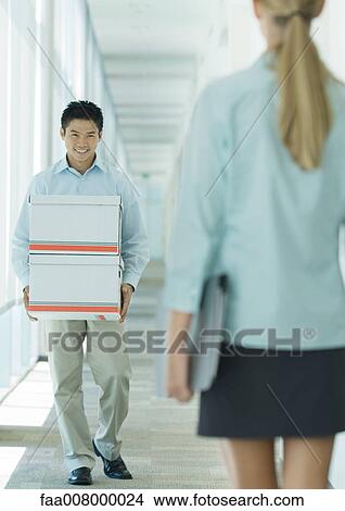 Man carrying boxes in hallway, smiling at female colleague View Large Photo Image Picture - Man carrying boxes in hallway, smiling at female colleague. Fotosearch
