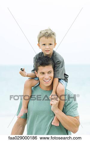 Man carrying son on his shoulders, boy holding seashell, both smiling View Large Photo Image Stock Photograph - Man carrying son on his shoulders, boy holding seashell, both smiling. Fotosearch