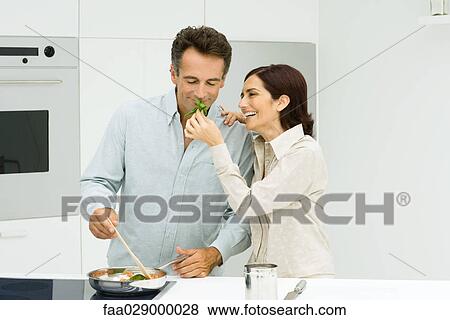 Stock Photo - Man cooking, woman holding up basil for man to smell. Fotosearch