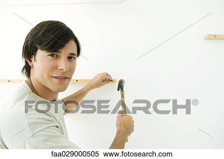 Stock Photography - Man holding hammer and wooden post, smiling over shoulder at camera. Fotosearch