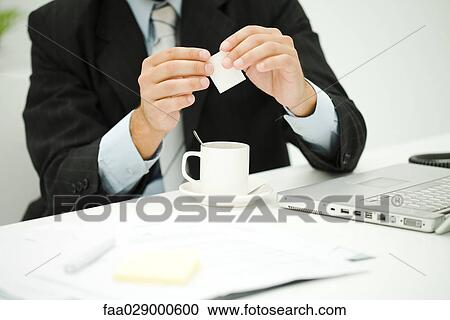 Stock Image - Man holding sugar packet over coffee cup, cropped view. Fotosearch