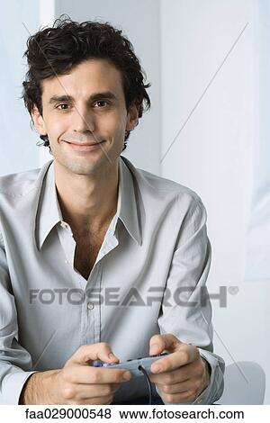 Man holding video game controller, smiling at camera View Large Photo Image Stock Photo - Man holding video game controller, smiling at camera. Fotosearch