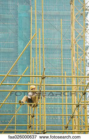 Man in hard hat perched on scaffolding, building in background View Large Photo Image Stock Photo - Man in hard hat perched on scaffolding, building in background. Fotosearch