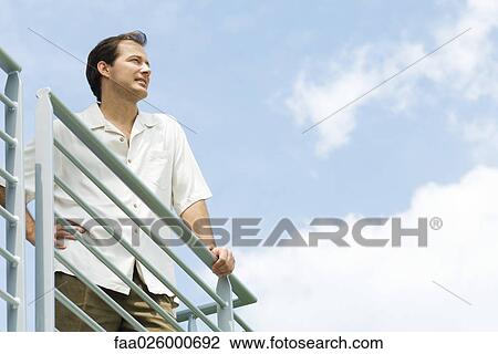 Man leaning against railing, looking into distance, low angle view View Large Photo Image Stock Image - Man leaning against railing, looking into distance, low angle view. Fotosearch