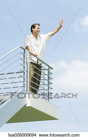 Man leaning against railing, waving, low angle view View Large Photo Image Picture - Man leaning against railing, waving, low angle view. Fotosearch