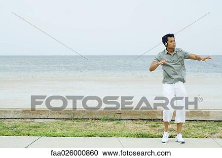 Man listening to headphones at the beach, dancing, looking away View Large Photo Image Stock Image - Man listening to headphones at the beach, dancing, looking away. Fotosearch