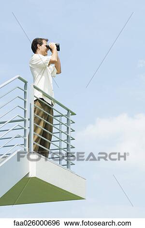 Man looking through binoculars, low angle view View Large Photo Image Stock Photograph - Man looking through binoculars, low angle view. Fotosearch