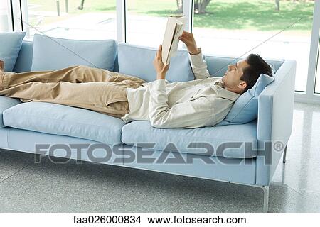 Man lying on sofa, reading book, side view View Large Photo Image Picture - Man lying on sofa, reading book, side view. Fotosearch