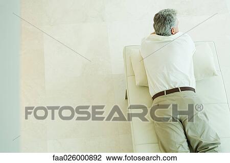 Stock Image - Man lying on stomach on chaise longue, high angle view. Fotosearch