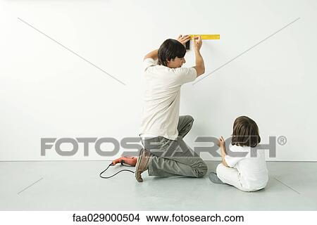 Man measuring wall with a ruler while his son watches, drill on the floor nearby View Large Photo Image Picture - Man measuring wall with a ruler while his son watches, drill on the floor nearby. Fotosearch