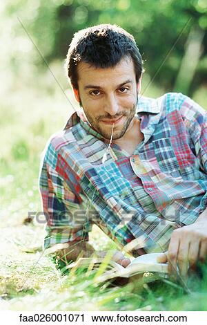 Man reading book outdoors, smiling at camera, blade of grass in mouth View Large Photo Image Stock Image - Man reading book outdoors, smiling at camera, blade of grass in mouth. Fotosearch
