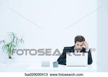 Man sitting at desk, using laptop, holding head View Large Photo Image Stock Image - Man sitting at desk, using laptop, holding head. Fotosearch