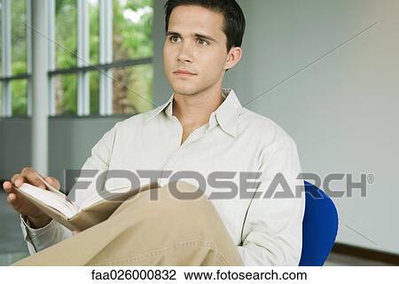 Man sitting in chair, holding book, looking away View Large Photo Image Stock Image - Man sitting in chair, holding book, looking away. Fotosearch