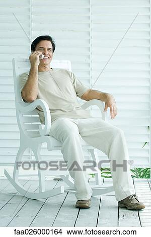 Man sitting in rocking chair, using cell phone, full length View Large Photo Image Picture - Man sitting in rocking chair, using cell phone, full length. Fotosearch