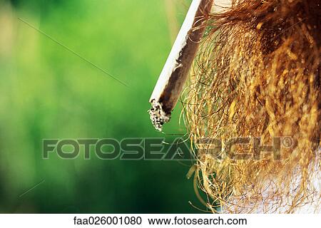 Stock Image - Man smoking hand-rolled cigarette, extreme close-up. Fotosearch