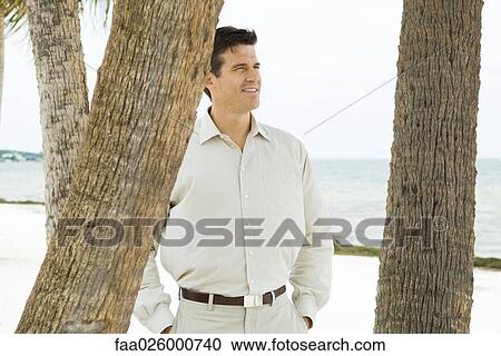 Man standing among palm trees, smiling, sea in background View Large Photo Image Stock Image - Man standing among palm trees, smiling, sea in background. Fotosearch