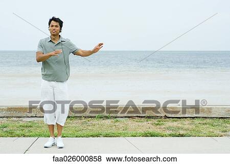 Man standing at the beach with arms out, listening to headphones, smiling at camera View Large Photo Image Stock Photo - Man standing at the beach with arms out, listening to headphones, smiling at camera. Fotosearch