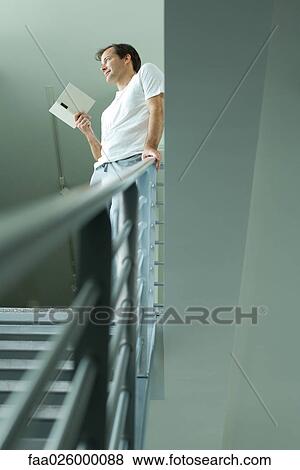 Man standing at top of staircase, holding book, looking away View Large Photo Image Stock Photo - Man standing at top of staircase, holding book, looking away. Fotosearch
