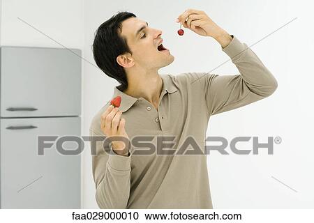 Man standing in kitchen, eating berries View Large Photo Image Stock Image - Man standing in kitchen, eating berries. Fotosearch