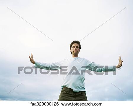 Stock Photograph - Man standing outdoors with arms outstretched, low angle view. Fotosearch