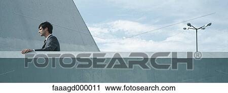 Stock Image - Man standing outside with hand on concrete railing. Fotosearch