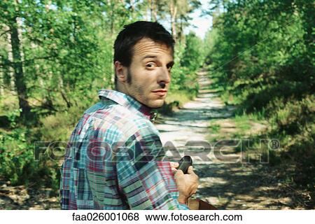 Stock Photo - Man walking on path in woods, looking over shoulder at camera, close-up. Fotosearch