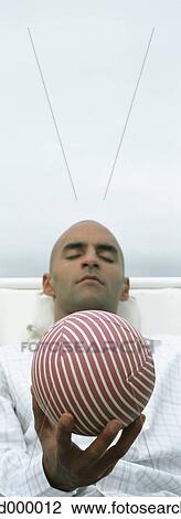 Stock Image - Man with eyes closed holding ball. Fotosearch