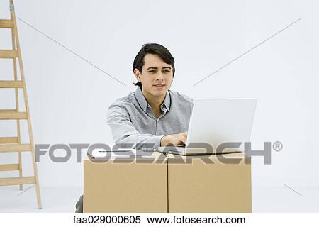 Man working on laptop computer, using cardboard boxes as makeshift desk View Large Photo Image Stock Photography - Man working on laptop computer, using cardboard boxes as makeshift desk. Fotosearch