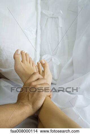 Picture - Man's hand holding woman's ankle in bed. Fotosearch