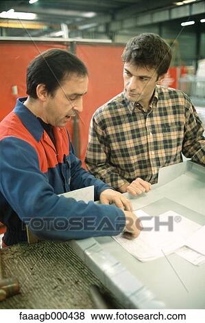 Stock Photo - Manual worker and apprentice at work table. Fotosearch