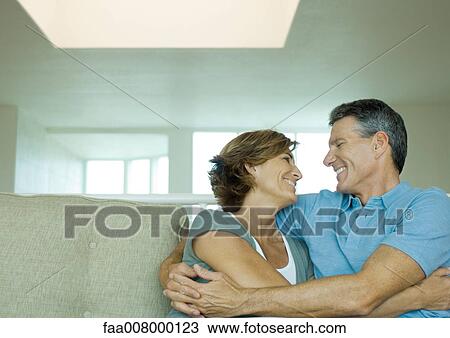 Stock Image - Mature couple embracing on sofa. Fotosearch