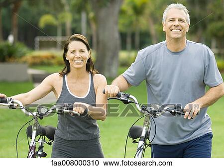 Mature couple standing next to bikes, smiling View Large Photo Image Stock Image - Mature couple standing next to bikes, smiling. Fotosearch