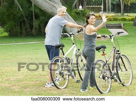 Mature couple walking with bikes, woman waving to camera View Large Photo Image Stock Photo - Mature couple walking with bikes, woman waving to camera. Fotosearch