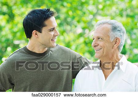 Mature man and adult son looking at each other, smiling View Large Photo Image Stock Photo - Mature man and adult son looking at each other, smiling. Fotosearch