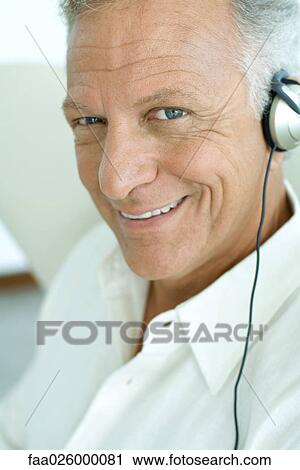 Mature man listening to headphones, smiling at camera, close-up View Large Photo Image Stock Image - Mature man listening to headphones, smiling at camera, close-up. Fotosearch