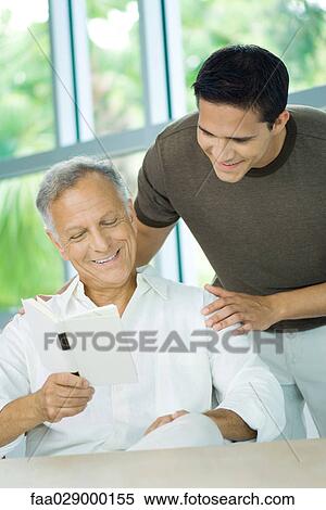 Mature man reading book, adult son looking over his shoulder, both smiling View Large Photo Image Stock Photography - Mature man reading book, adult son looking over his shoulder, both smiling. Fotosearch