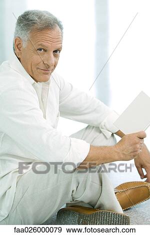 Mature man sitting indian style, holding book, smiling at camera View Large Photo Image Stock Photo - Mature man sitting indian style, holding book, smiling at camera. Fotosearch