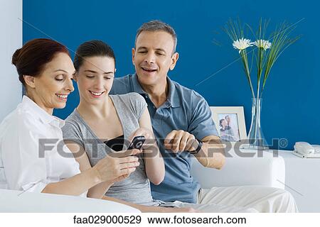 Mature parents and teen daughter looking at cell phone together, smiling View Large Photo Image Stock Photo - Mature parents and teen daughter looking at cell phone together, smiling. Fotosearch