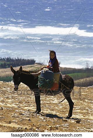 Stock Photograph - Morocco, girl on donkey overlooking sea. Fotosearch