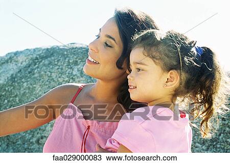 Stock Image - Mother and daughter looking away outdoors, smiling, side view. Fotosearch