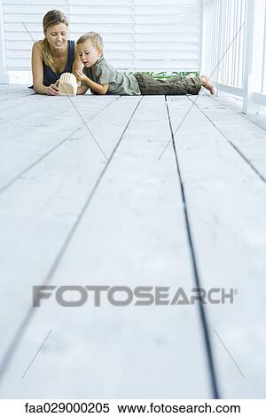Stock Photography - Mother and son lying on deck, looking at wooden object, low angle view. Fotosearch