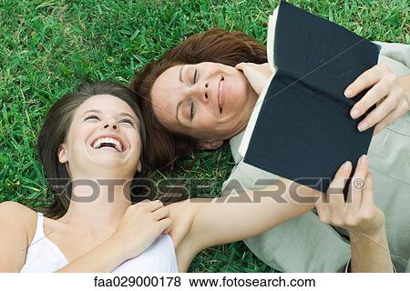 Mother and teen daughter lying together in grass, laughing, woman holding book View Large Photo Image Stock Photo - Mother and teen daughter lying together in grass, laughing, woman holding book. Fotosearch