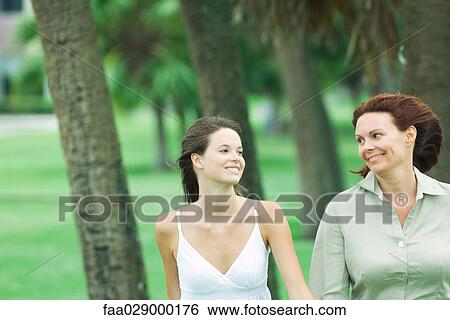 Mother and teen daughter walking together outdoors, smiling at each other View Large Photo Image Stock Photograph - Mother and teen daughter walking together outdoors, smiling at each other. Fotosearch