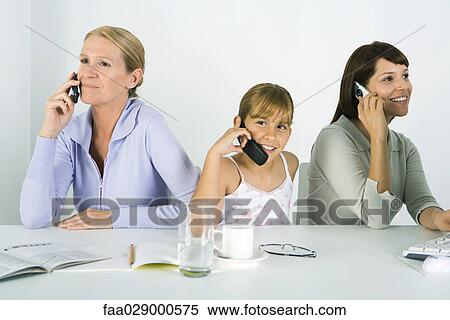 Mother and two daughters sitting at table, each using cell phone, smiling View Large Photo Image Stock Photography - Mother and two daughters sitting at table, each using cell phone, smiling. Fotosearch