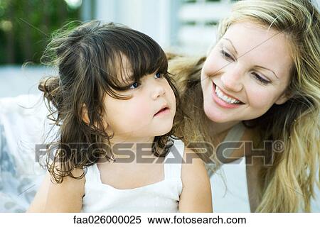 Mother looking over daughter's shoulder, smiling, close-up View Large Photo Image Stock Photography - Mother looking over daughter's shoulder, smiling, close-up. Fotosearch