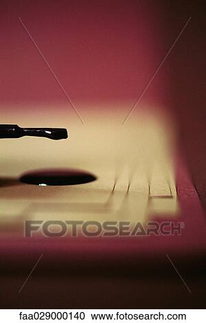 Stock Image - Nail polish dripping from brush onto papers, close-up. Fotosearch