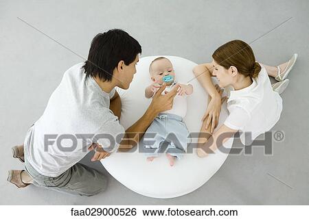 New parents crouching next to infant, high angle view View Large Photo Image Stock Photograph - New parents crouching next to infant, high angle view. Fotosearch