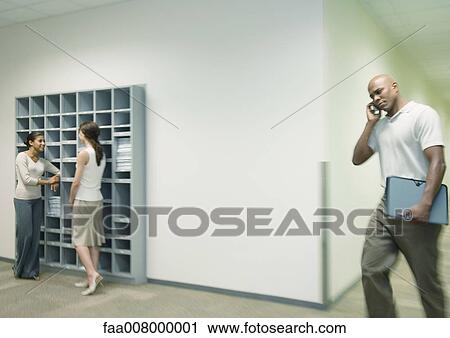 Office scene, two women talking by mailboxes while man using cell phone walks through hallway View Large Photo Image Stock Image - Office scene, two women talking by mailboxes while man using cell phone walks through hallway. Fotosearch